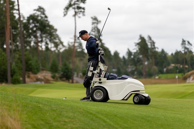 Paragolfari-nosto- ja kuljetusvälineen avulla seisova golfari lyömässä palloa viheriöllä.